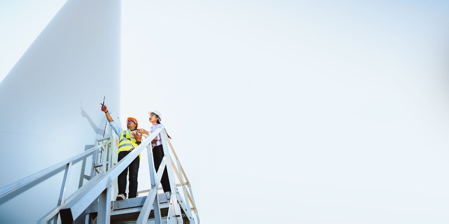 Two workers at the base of a wind turbine